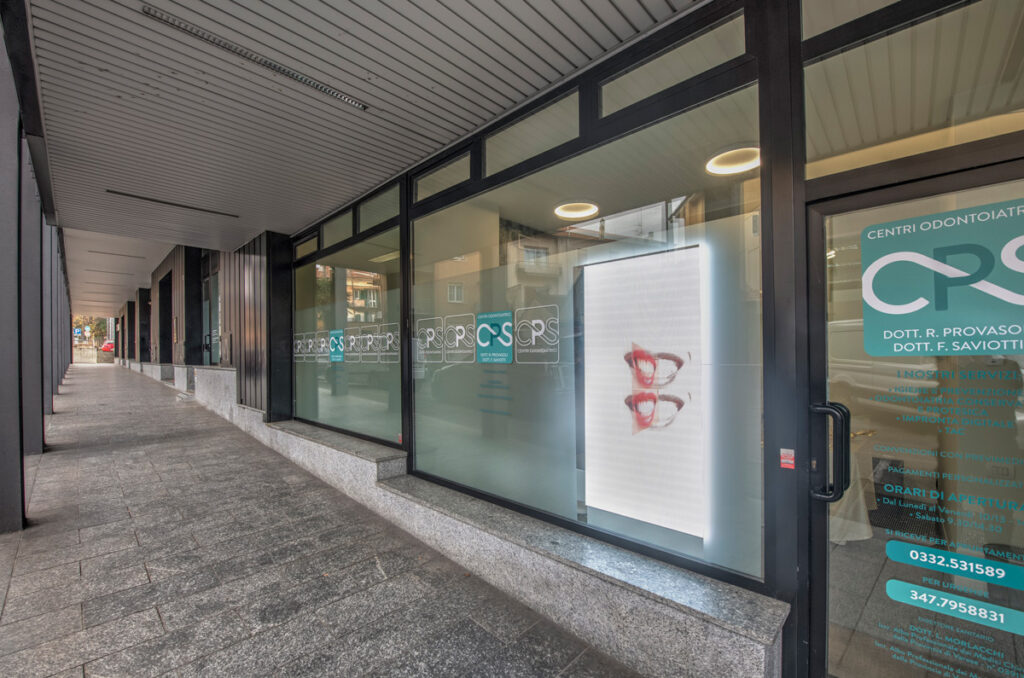 Vista esterna dello studio dentistico CPS Centri Odontoiatrici a Luino, con vetrine e insegna visibile sotto i portici.